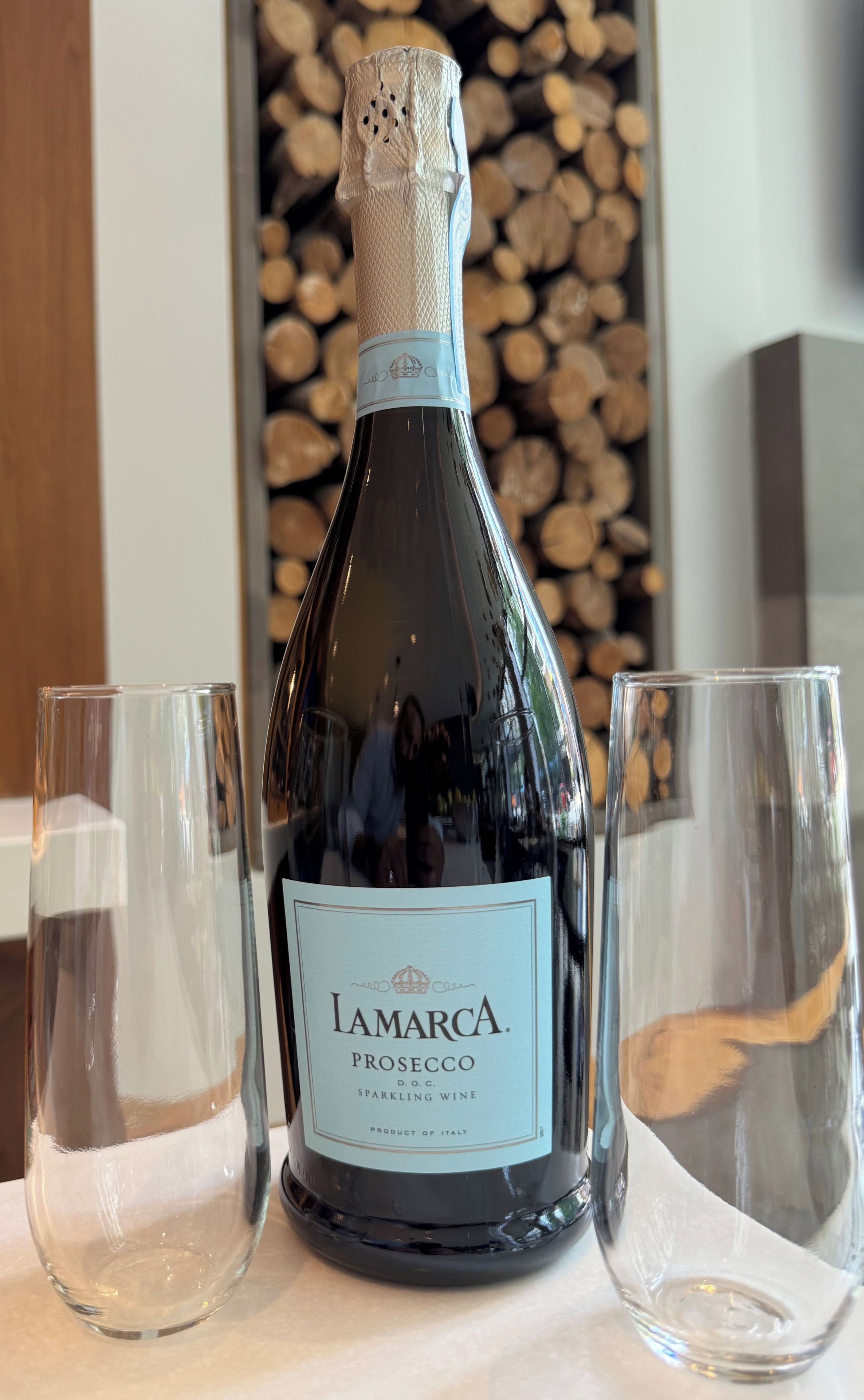 Una botella de vino espumoso Lamarca Prosecco con dos copas vacías a su lado.