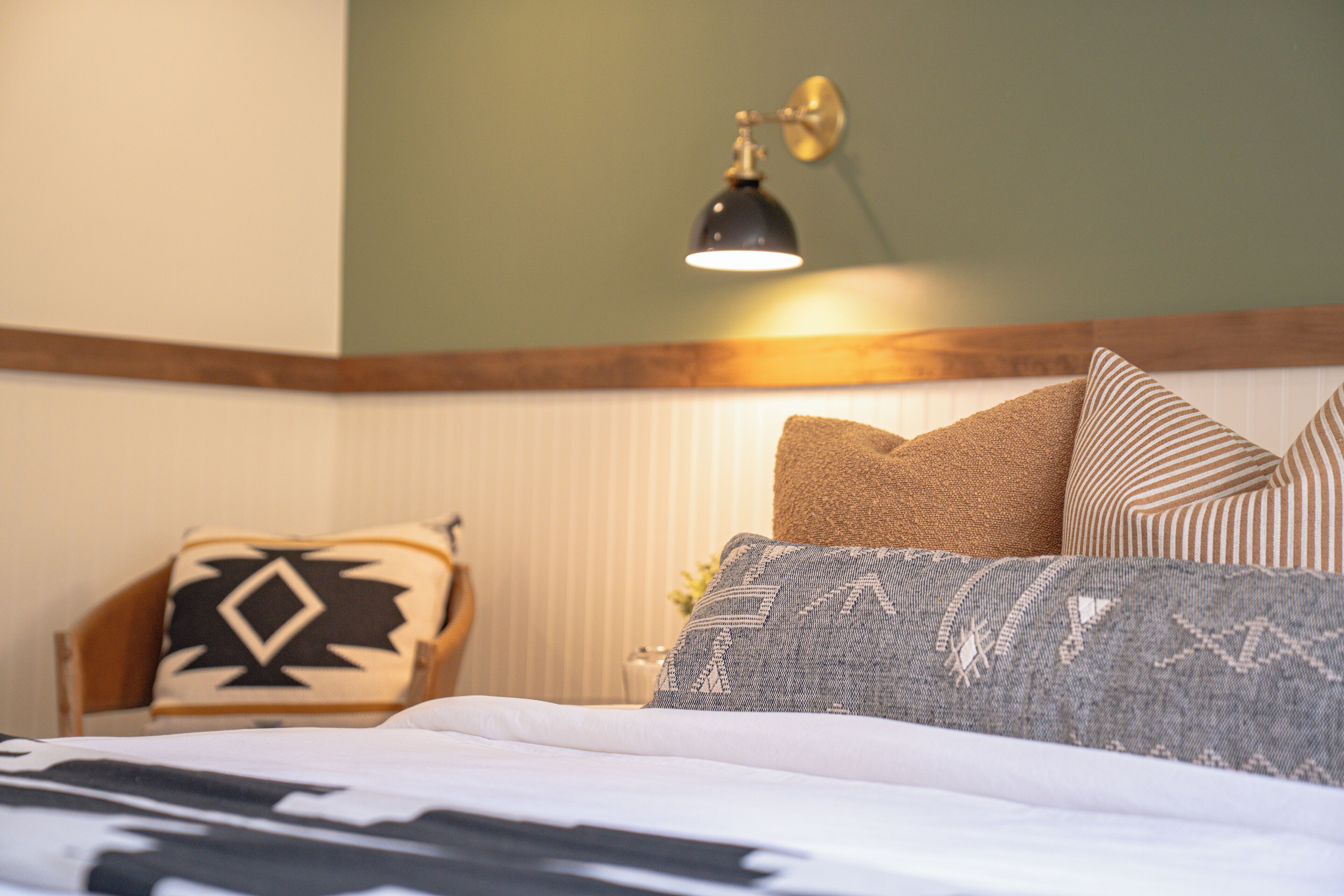 Un letto rifatto con cuscini decorati, una lampada a parete e una testiera in legno.