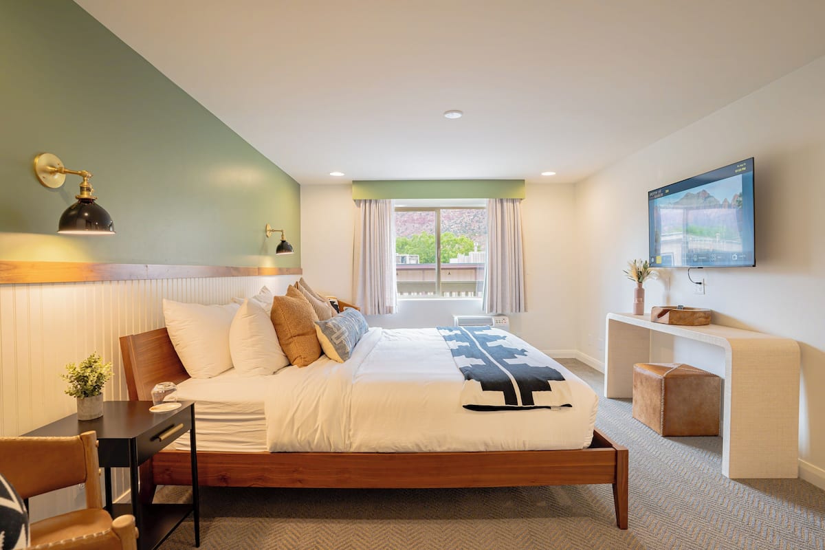 A modern hotel room with a large bed, bedside tables, a desk, and a TV mounted on the wall.