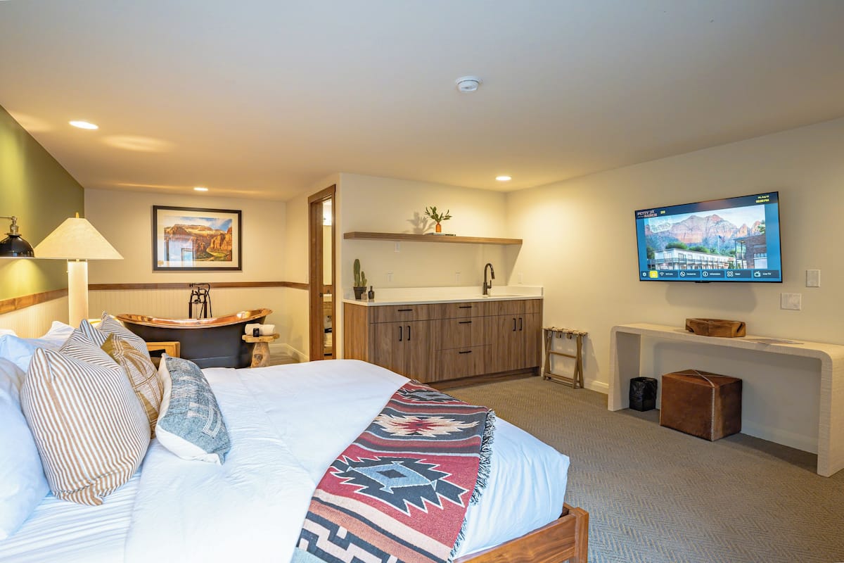 A hotel room with a bed, a desk, a sink, and a television.