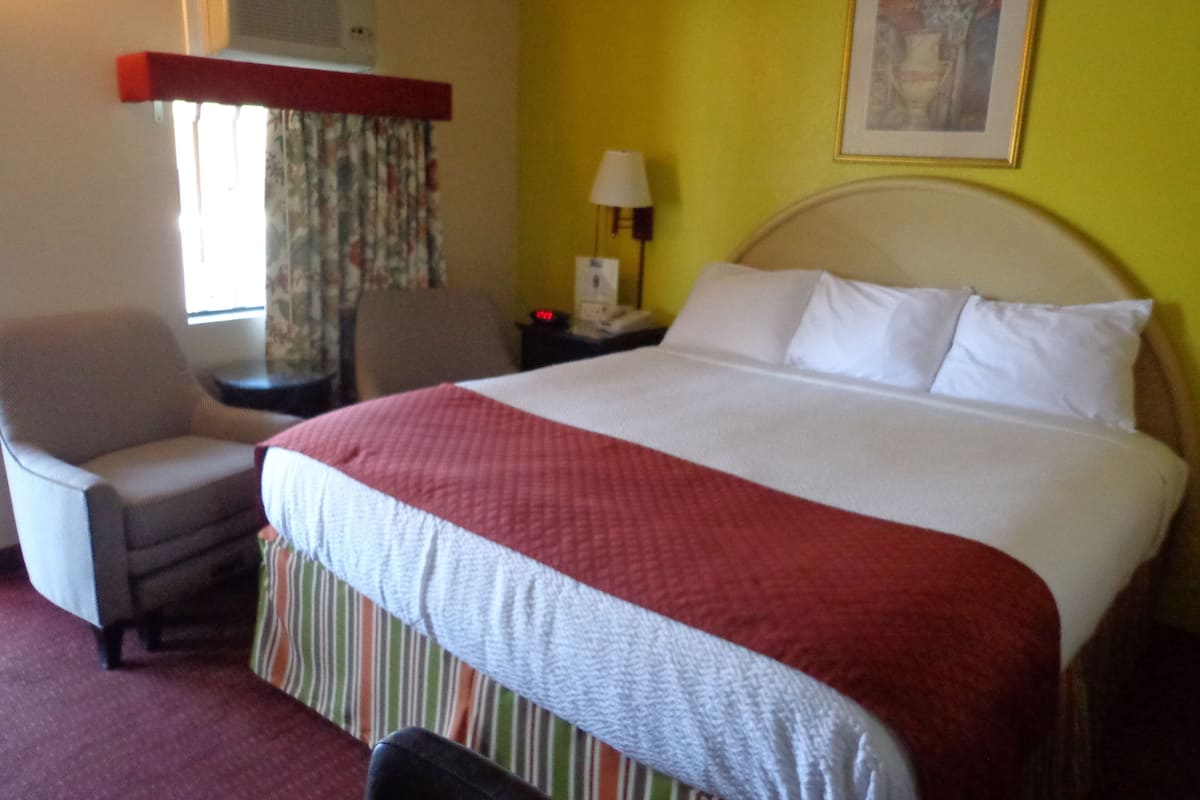 A hotel room with a bed, a chair, a nightstand, a lamp, and a window with curtains.
