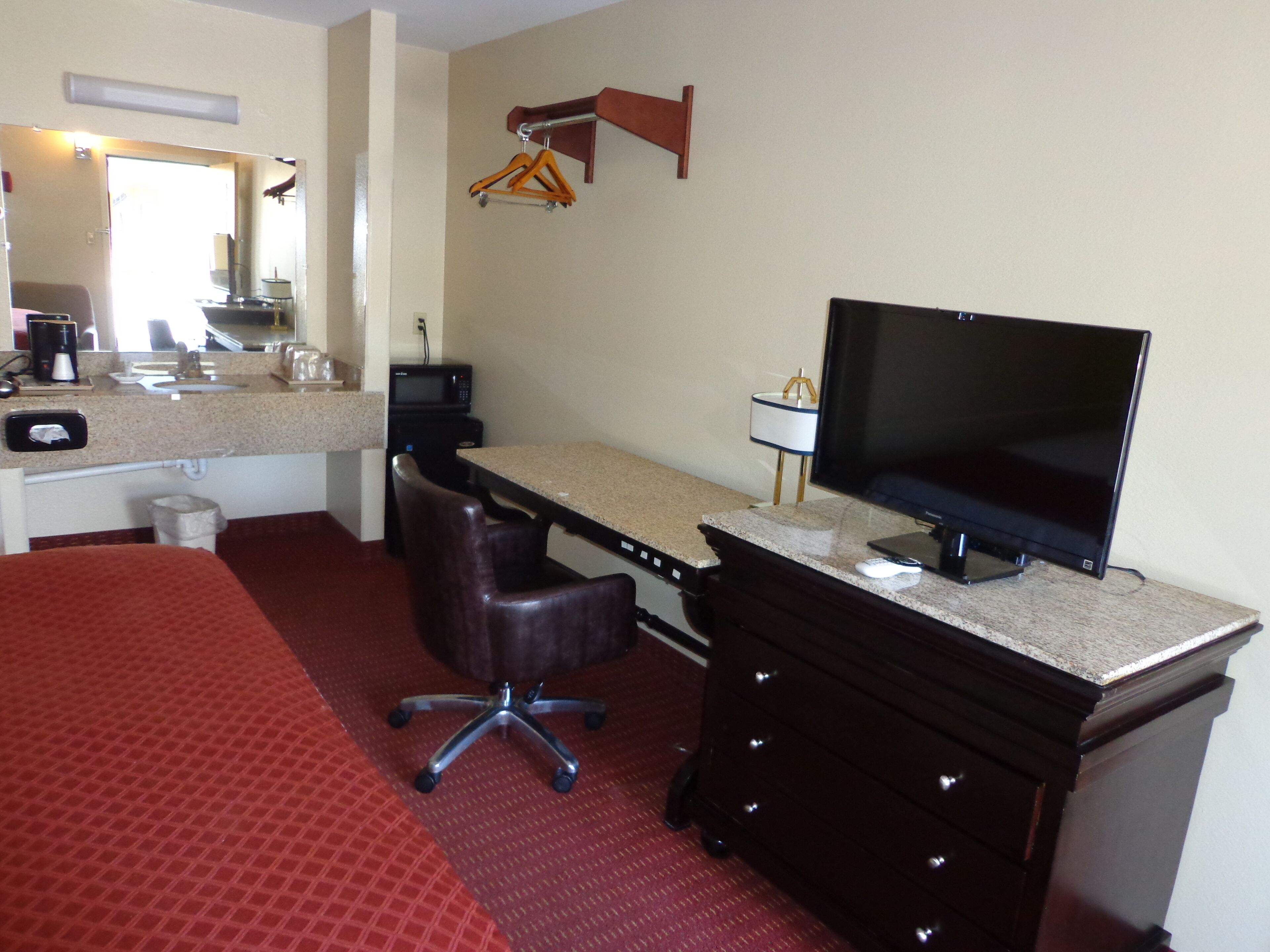 Habitación de hotel con cama, escritorio, silla, televisor y una pequeña cocina.