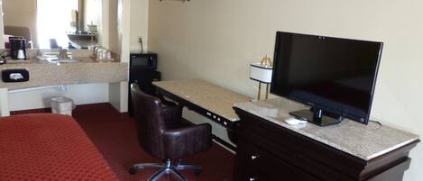 A hotel room with a bed, desk, chair, television, and a small kitchenette.