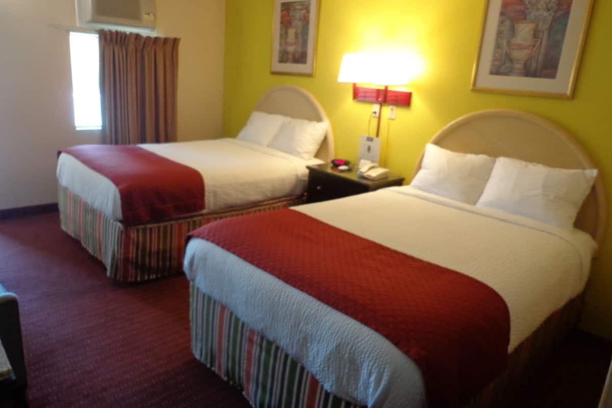 A hotel room with two beds, a nightstand, a lamp, and an air conditioning unit.