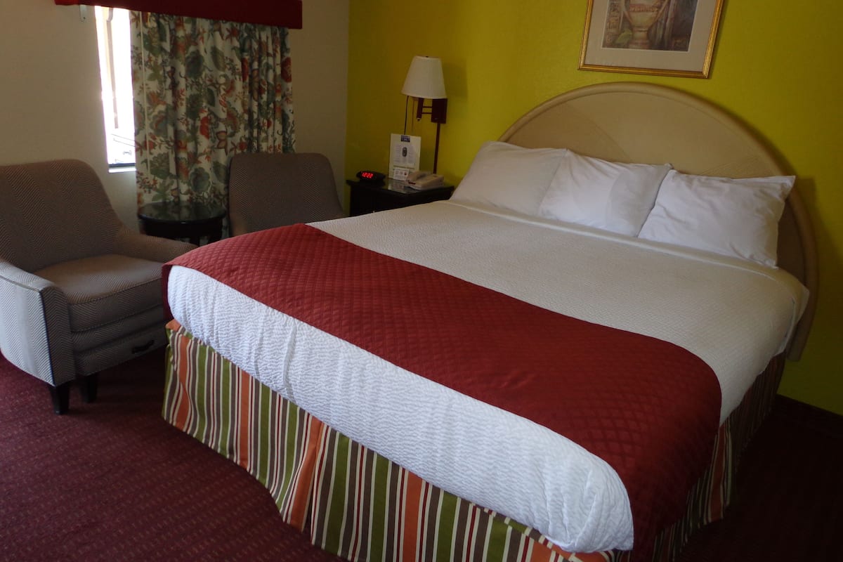 A hotel room with a bed, a chair, a nightstand, a lamp, and a window with curtains.