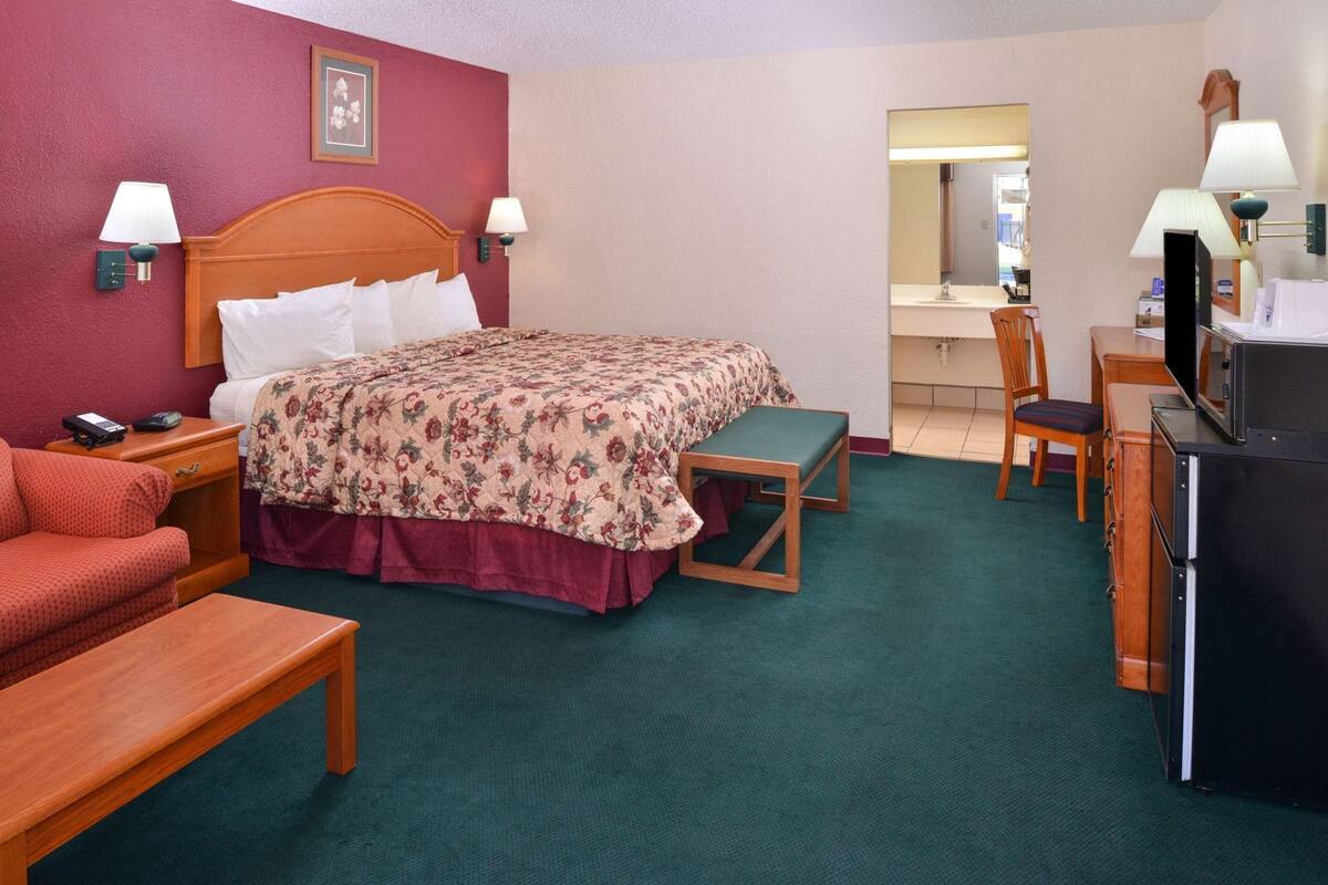A hotel room with a bed, a desk, a chair, a television, and a small table.
