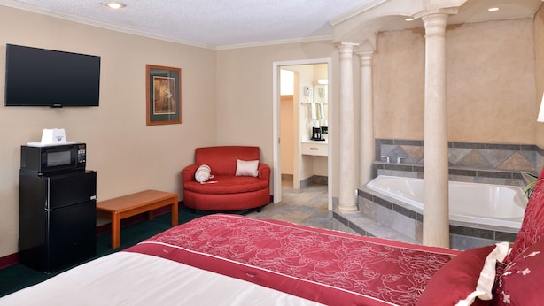 Ein Hotelzimmer mit einem Bett, einem roten Sessel, einem kleinen Schreibtisch mit einer Mikrowelle, einem Fernseher und einem Badezimmer mit einer Badewanne und einem Waschbecken.