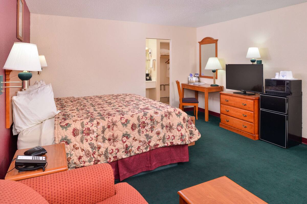 A hotel room with a bed, a desk, a television, a dresser, and a telephone.