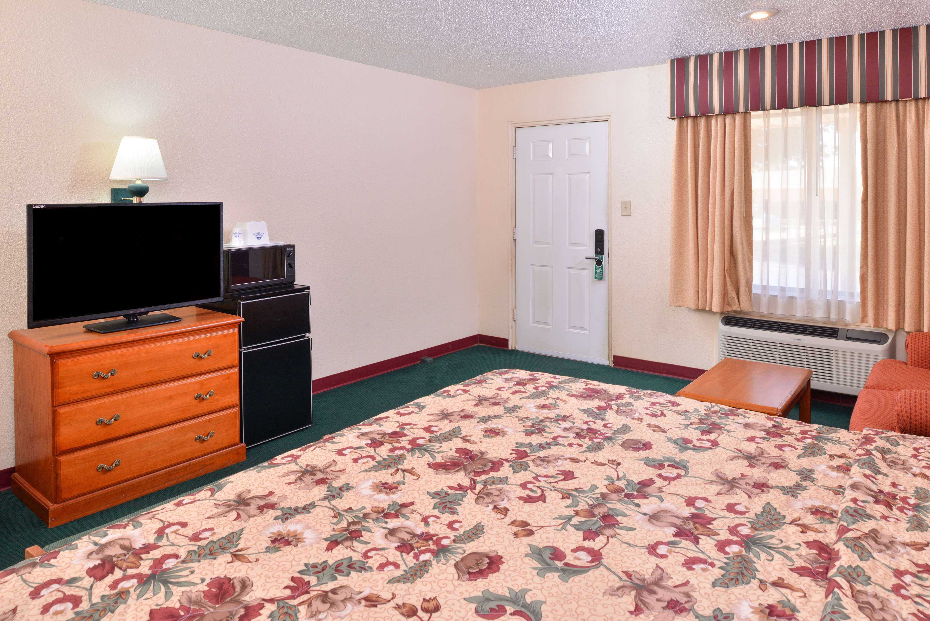 A hotel room with a bed, a dresser, a television, a microwave, and a door.