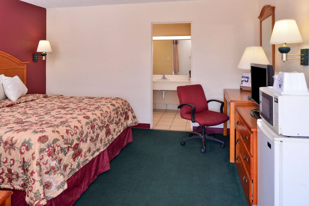 A hotel room with a bed, a desk with a computer, a chair, a dresser, and a microwave.