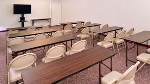 Ein Konferenzraum mit mehreren Tischen, Stühlen, einem Fernseher und einer Whiteboard-Tafel.