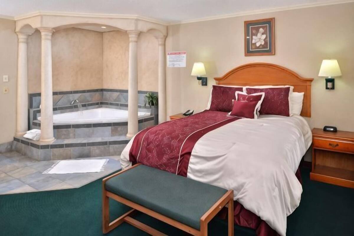 A hotel room with a bed, a bench, a bathtub, and two bedside lamps.