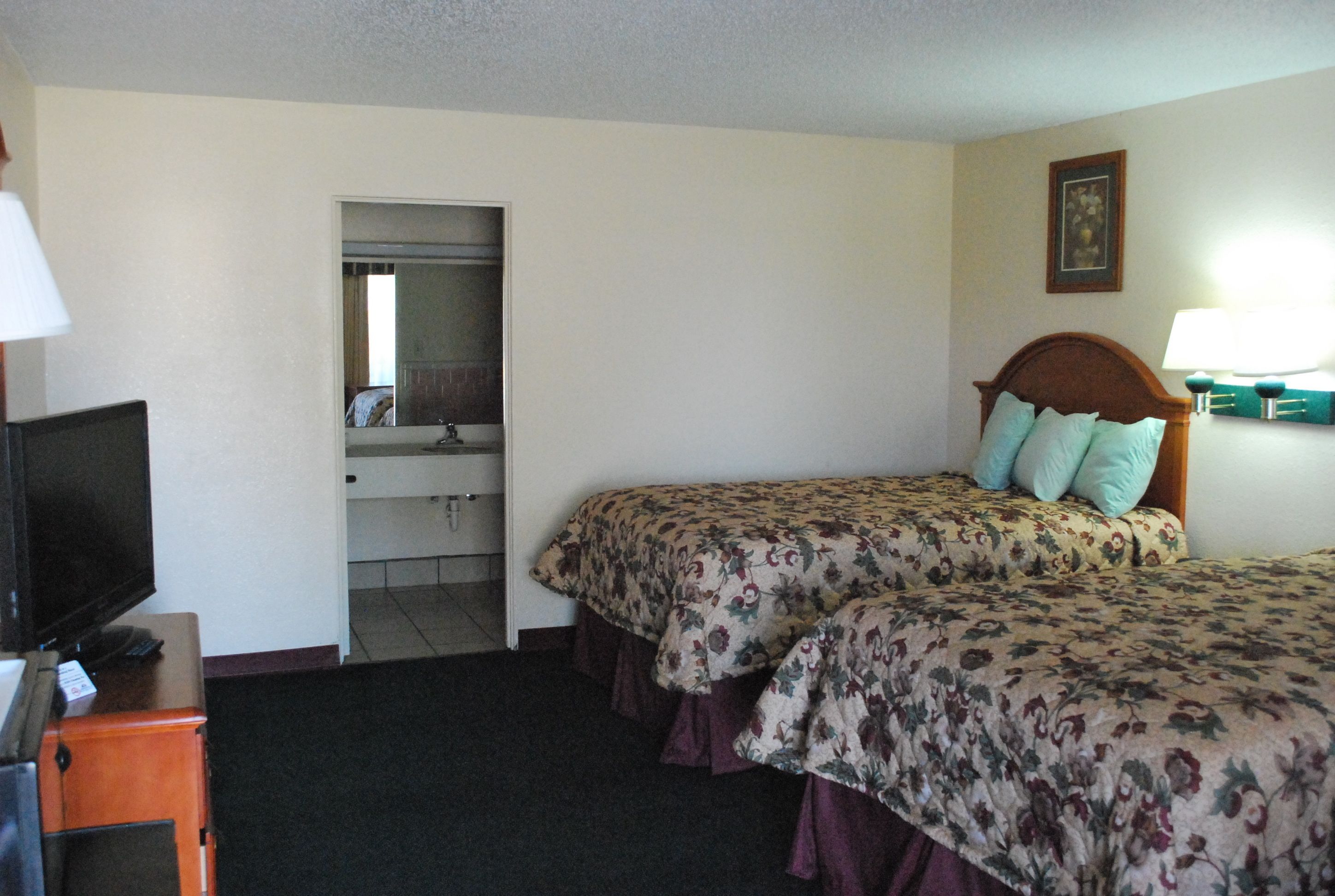 Une chambre d’hôtel avec deux lits, une télévision, un miroir, une commode et une salle de bain visible à travers une porte ouverte.
