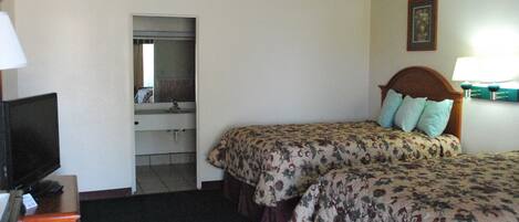 Une chambre d’hôtel avec deux lits, une télévision, un miroir, une commode et une salle de bain visible à travers une porte ouverte.