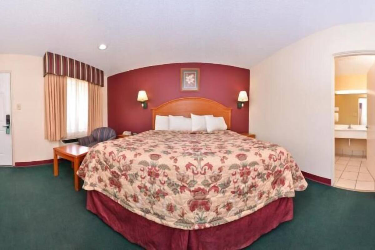 A hotel room with a bed, bedside table, lamp, chair, and a door.