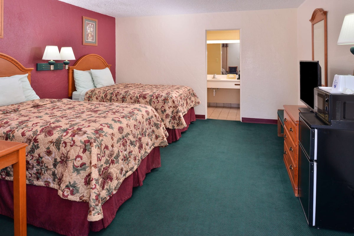 A hotel room with two beds, a desk, a dresser, a microwave, and a mirror.