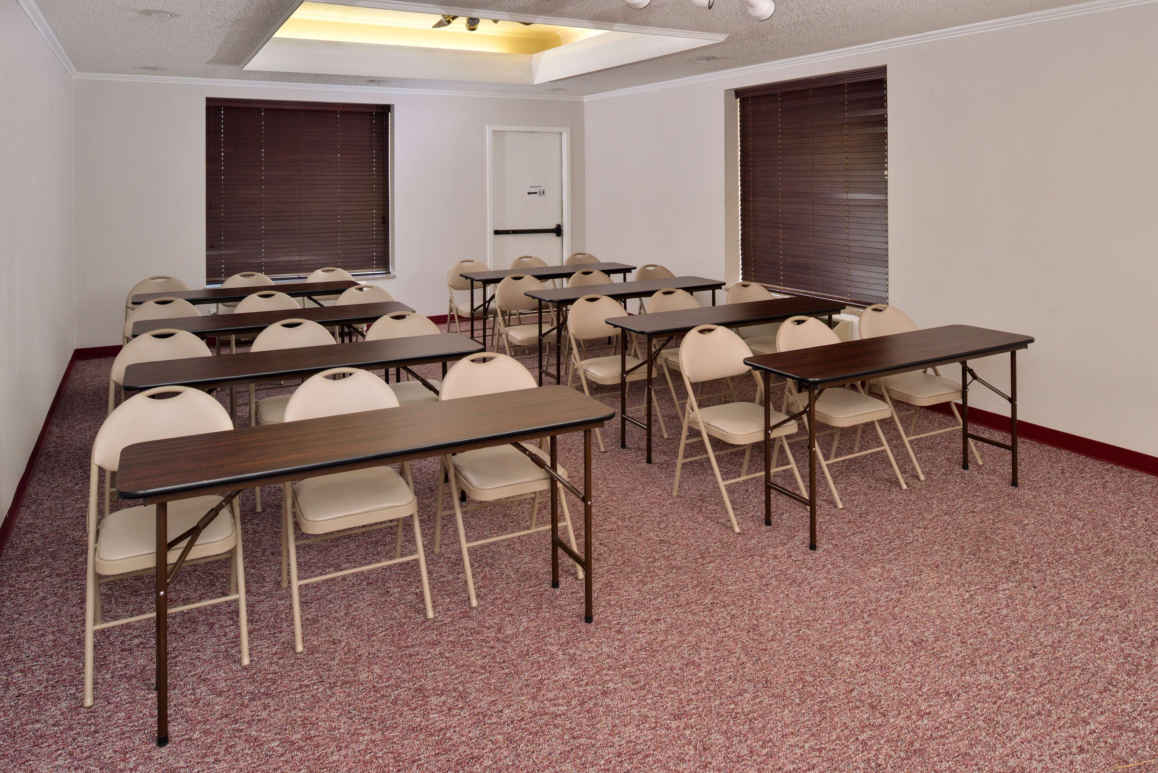 A conference room with multiple tables and chairs, carpeted floor, and windows with blinds.