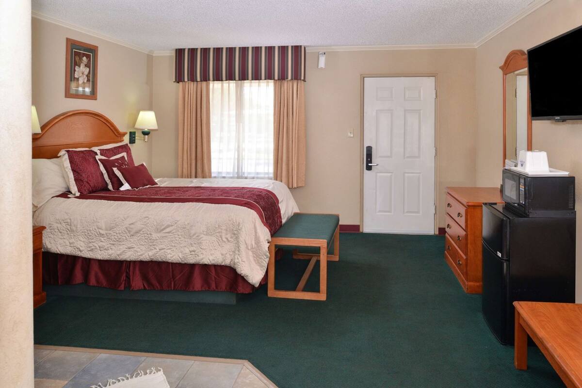 A hotel room with a bed, a desk, a television, a refrigerator, and a door.