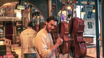 A person examining a cello in a room with a grid-like ceiling and hanging lights.