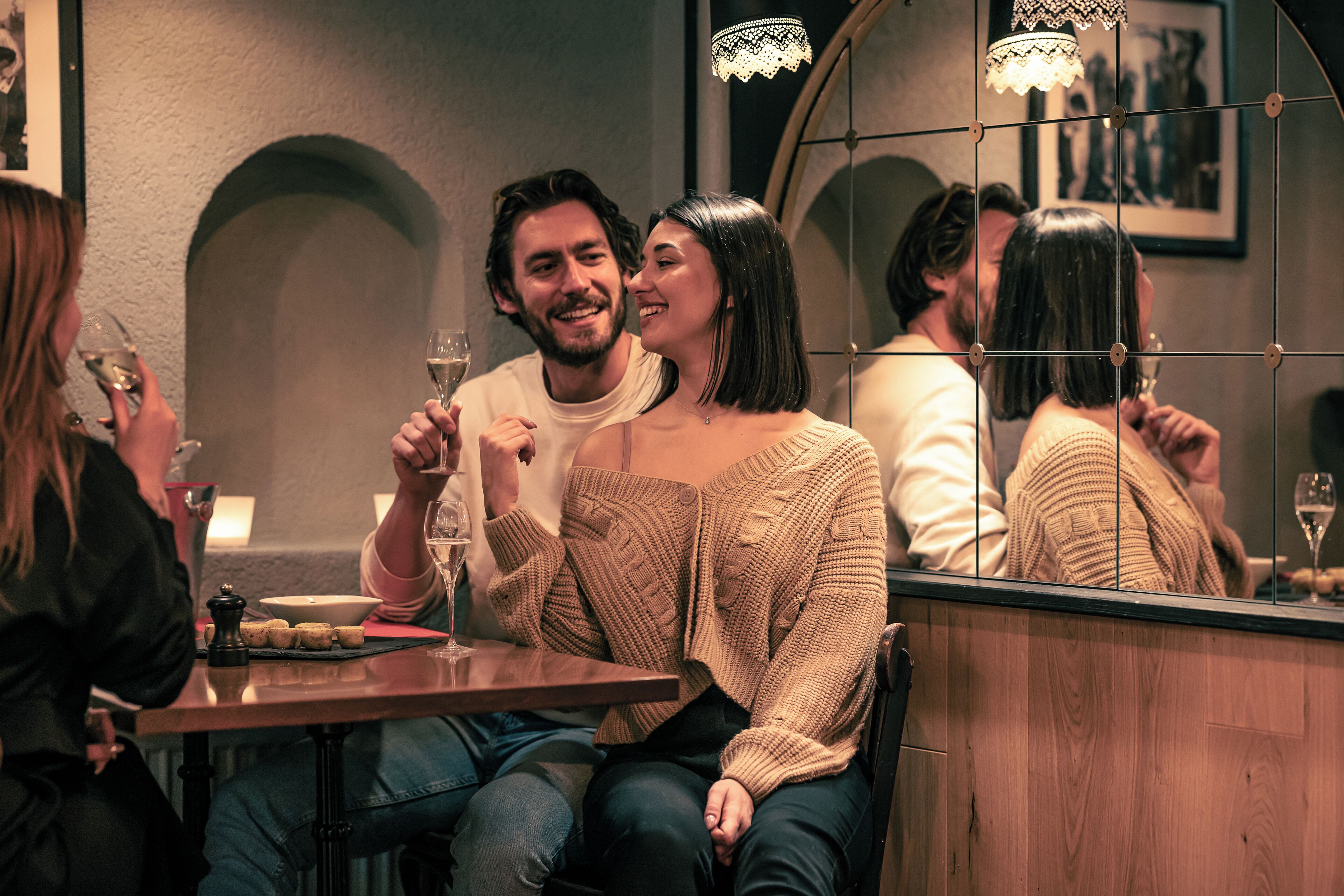 Un couple est assis à une table, devant un verre de vin, une bougie et une petite assiette de nourriture.