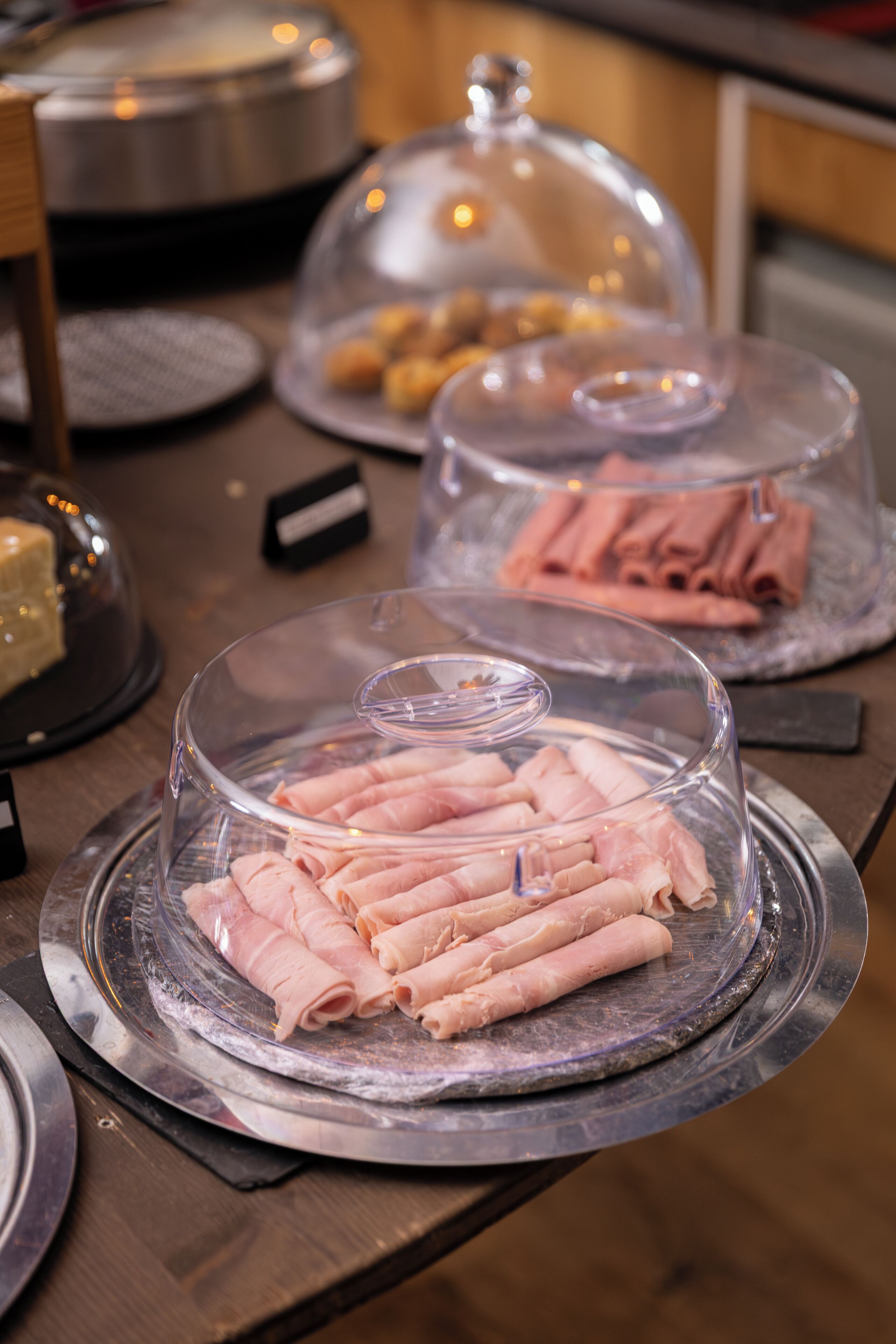 Un buffet proposant une variété de plats présentés sous cloche, notamment des viandes tranchées et des pâtisseries.