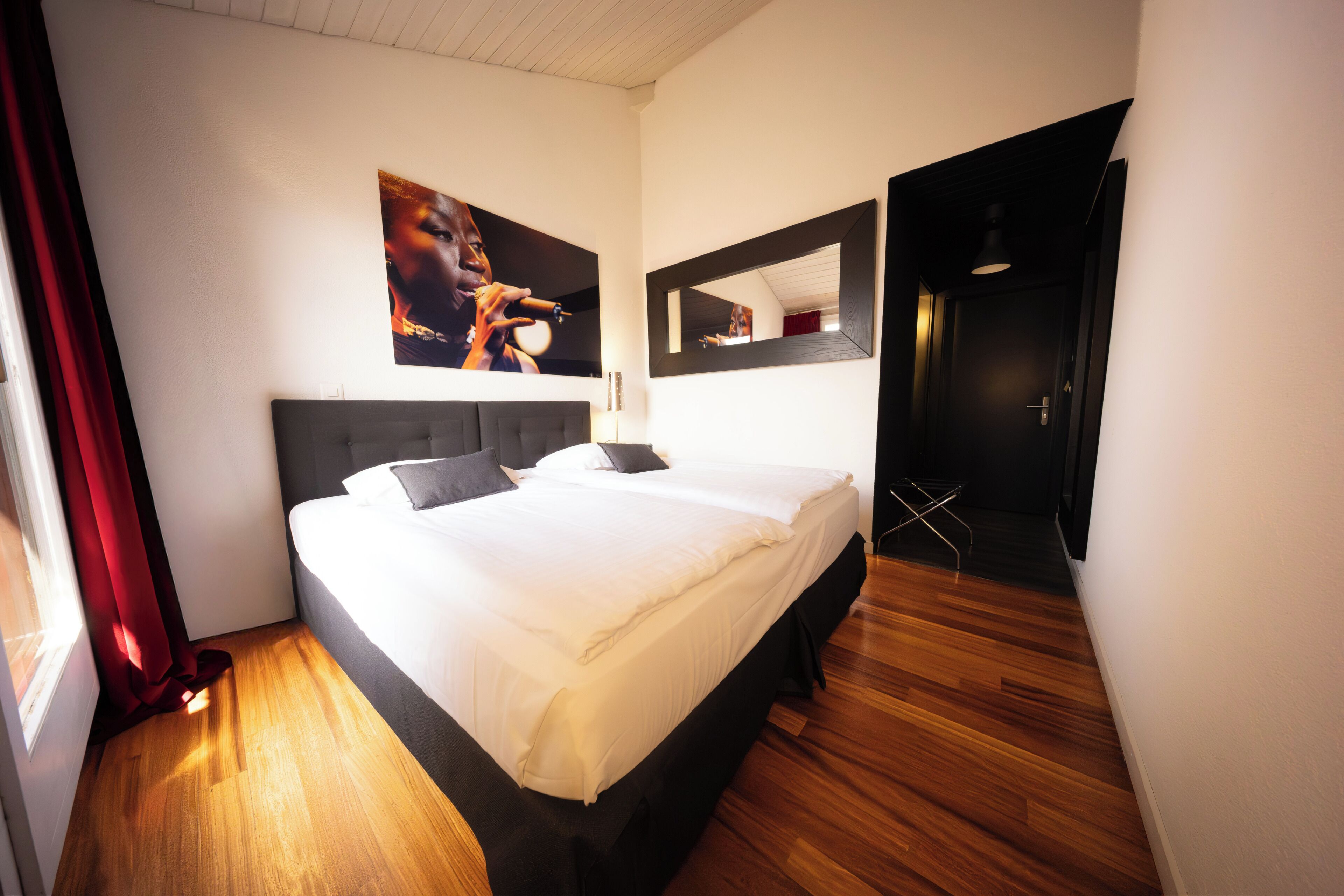 A hotel room with a large bed, a mirror, and a door leading to another room.