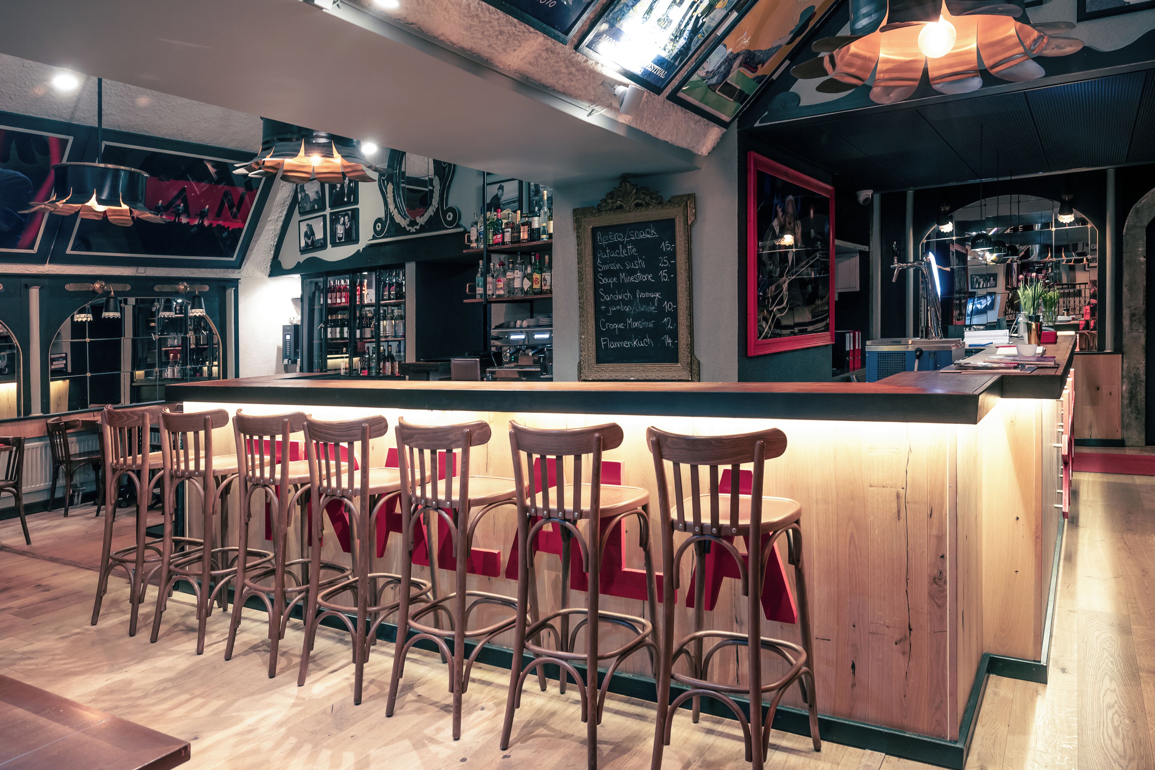 Eine Bar mit Holzhockern, einer Theke und Regalen mit Flaschen.