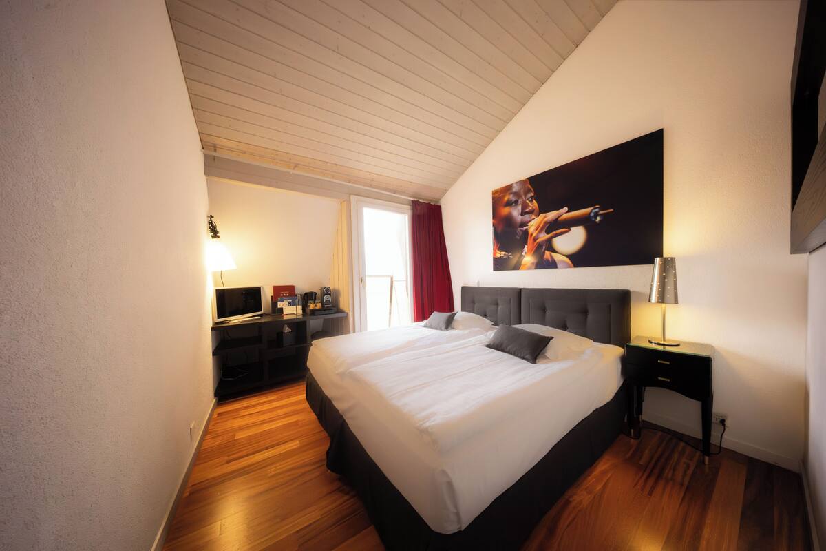 A hotel room with a large bed, a desk with a computer, a lamp, and a painting on the wall.