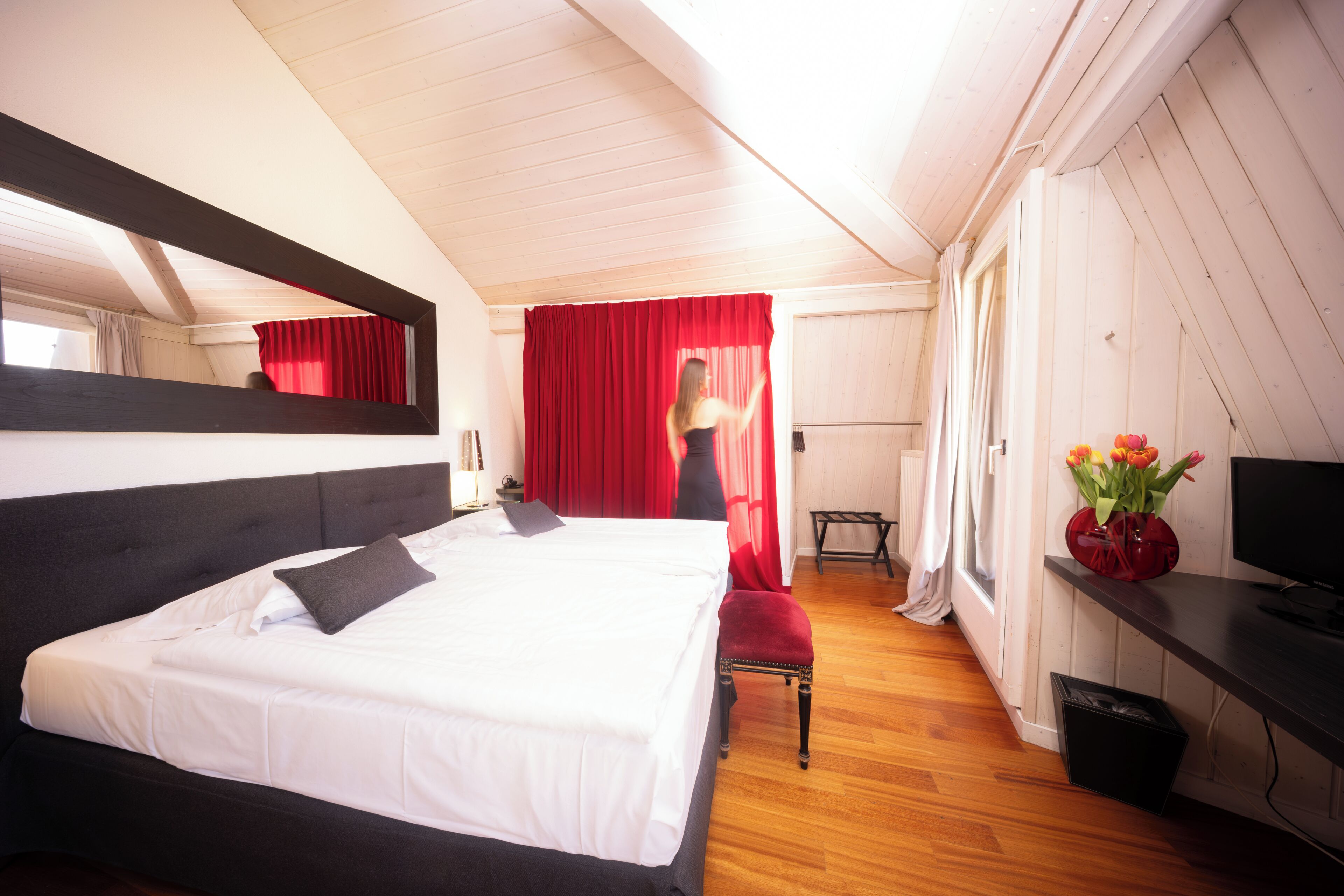 Een slaapkamer met een bed, een bureau, een stoel, een televisie en een raam met gordijnen.