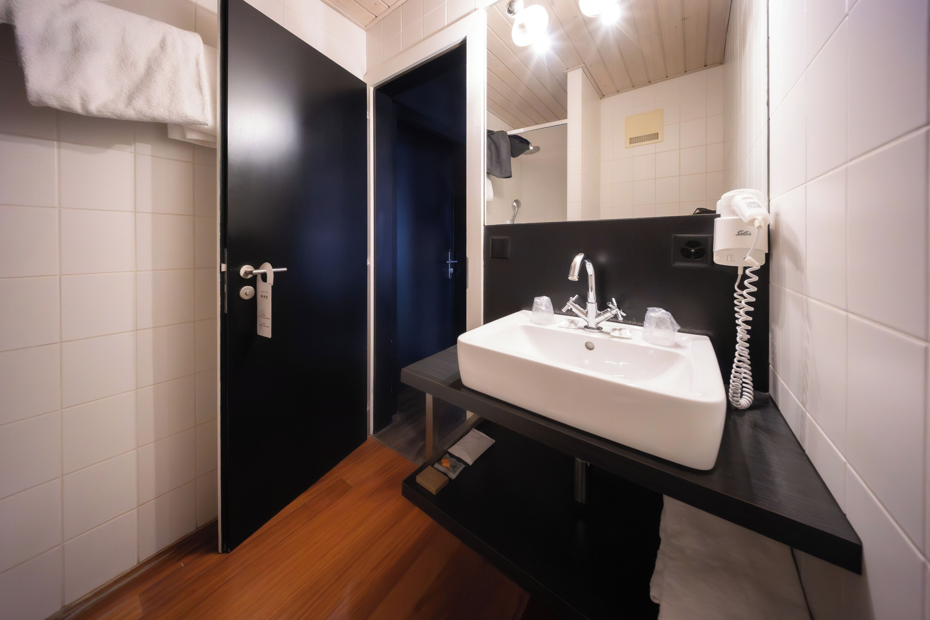 Un baño moderno con un lavamanos blanco, una encimera negra, un perchero y un espejo.