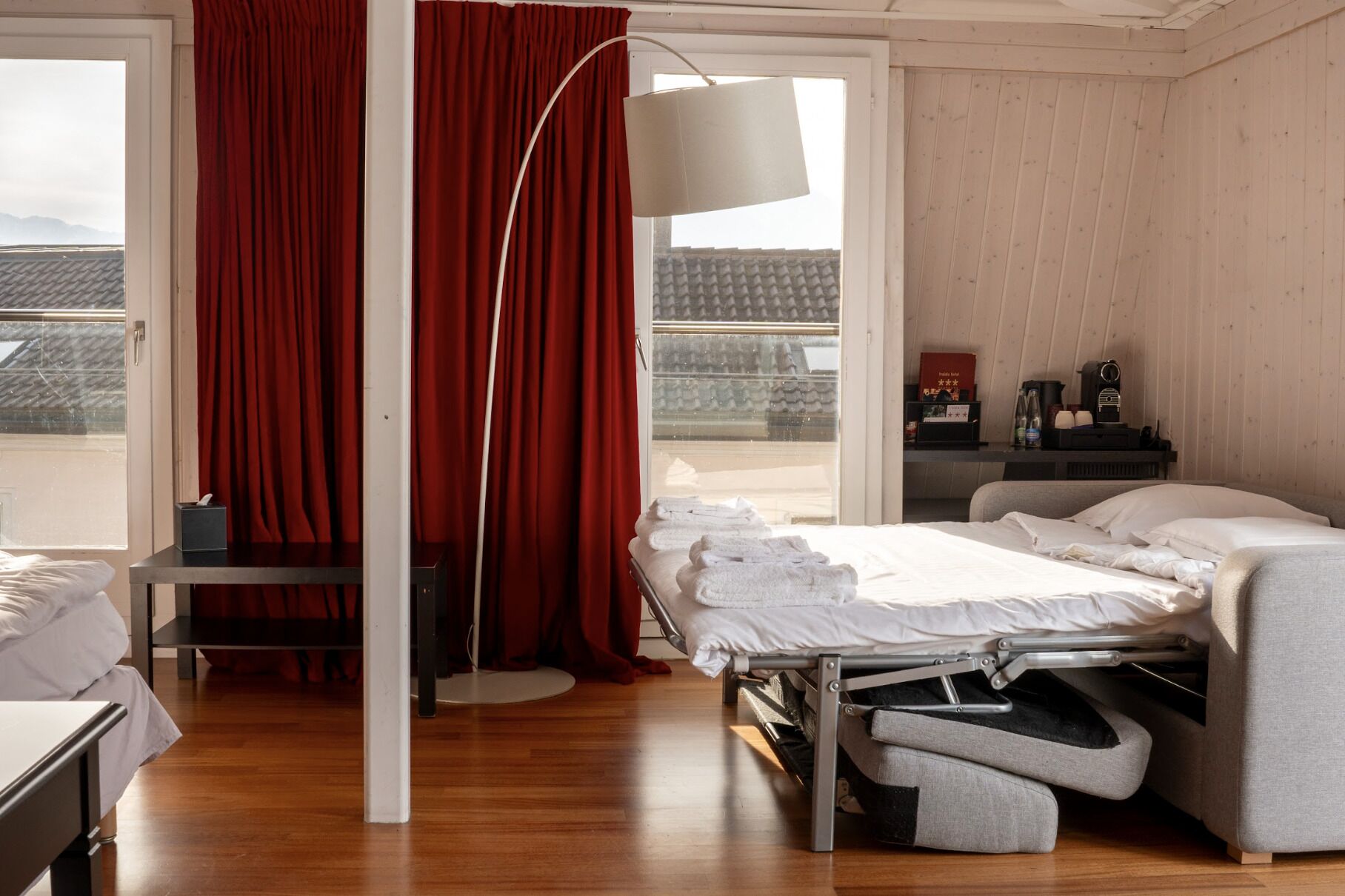 A modern hotel room with a bed, a desk, a chair, and a large window with curtains.