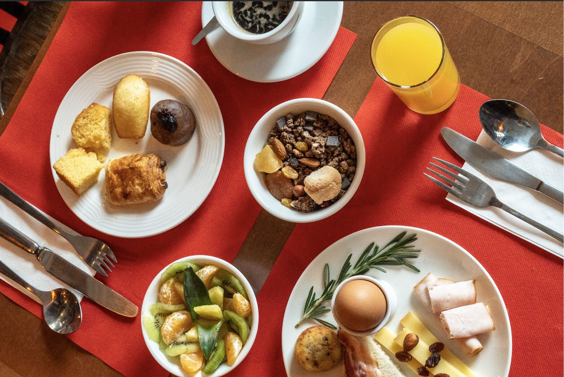 En frukostuppdukning med tallrikar fyllda med mat, en kopp kaffe och ett glas apelsinjuice.