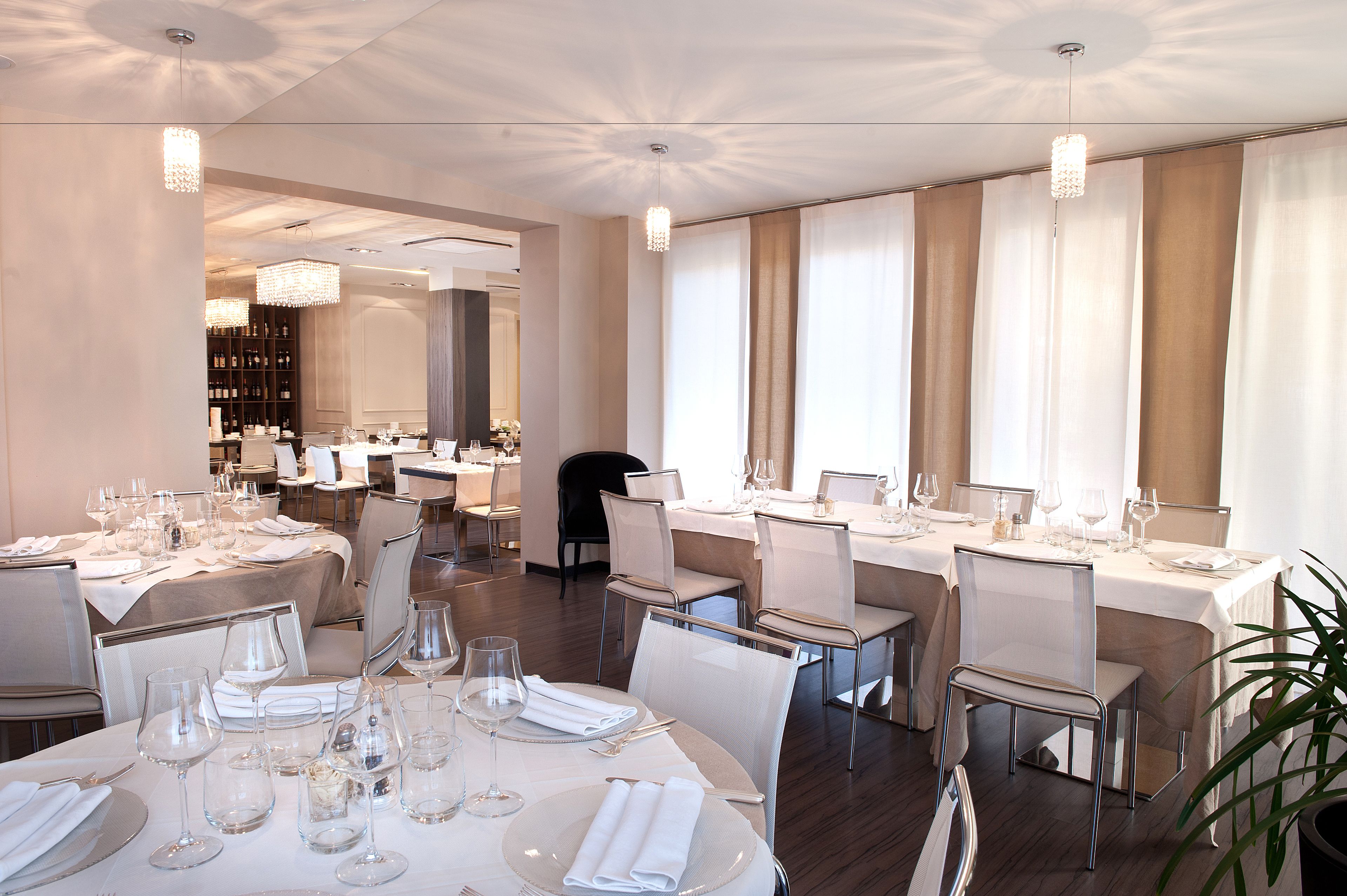 Una sala da pranzo ben illuminata con tavoli apparecchiati, sedie moderne e un lampadario.