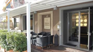 Ein Hotel Eingang mit einem Schild mit dem Schriftzug 'HOTEL CARLA', Sitzgelegenheiten im Freien mit Stühlen und Tischen sowie eine überdachte Terrasse.