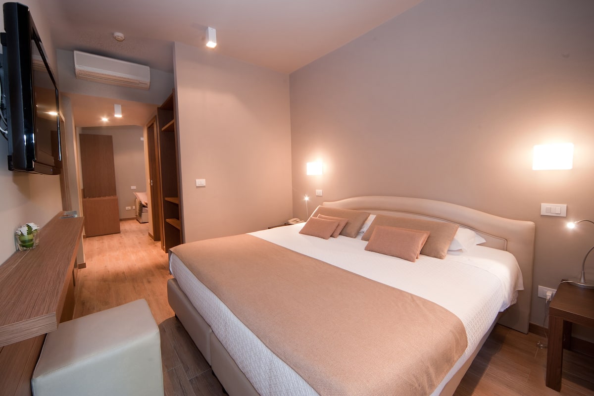 Un dormitorio moderno con una cama grande, mesitas de noche, un escritorio y un televisor.
