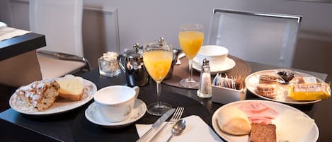 Una mesa de desayuno con diversas opciones de comida, como pasteles, sándwiches y un vaso de jugo de naranja.
