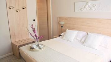 A neatly made bed with white bedding, a bedside table with a vase of pink flowers, and a wall-mounted artwork.