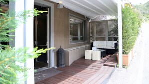 A covered outdoor seating area with a bench, a trash can, and a potted plant.