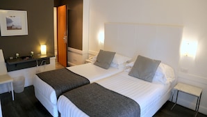 A hotel room with two beds, a small desk, a chair, a trash bin, and a picture on the wall.