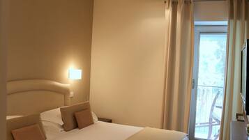 Habitación de hotel con una cama grande, una mesita de noche, una lámpara y vistas al exterior a través de una ventana.