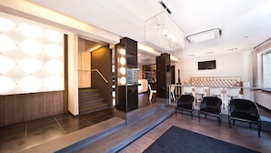 A modern hotel lobby with a staircase, seating area, and a chandelier.