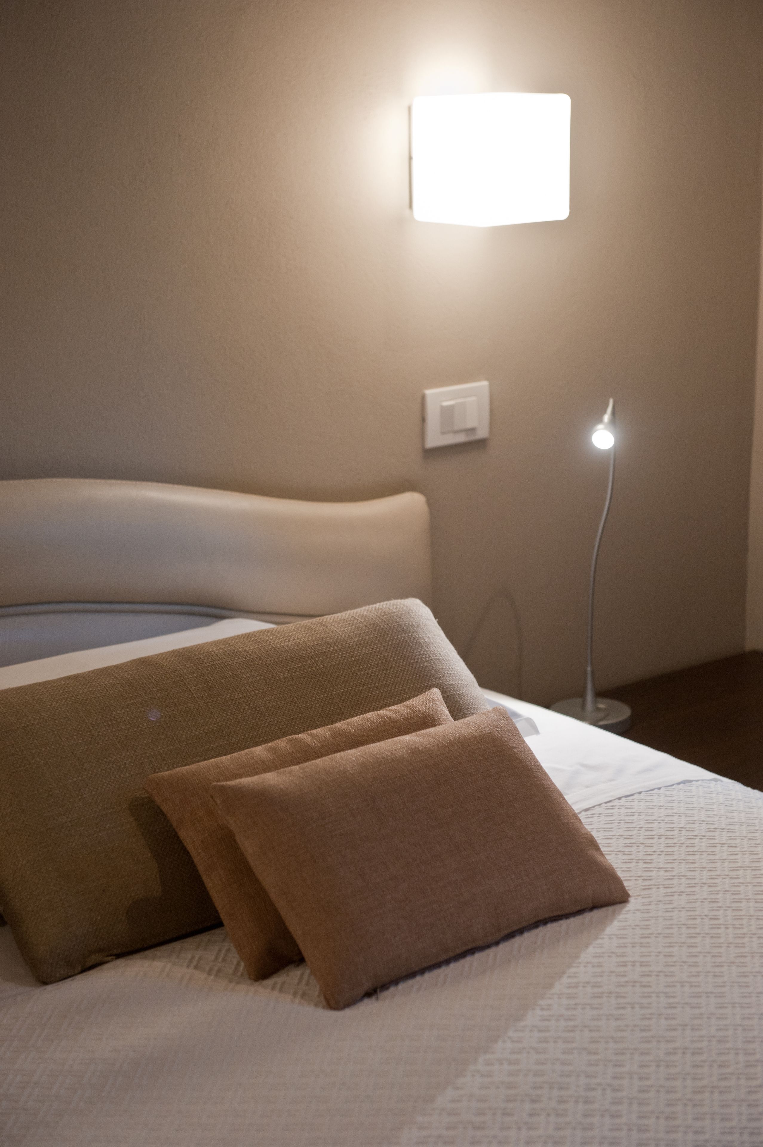 A neatly made bed with a white headboard, two beige pillows, and a bedside lamp.