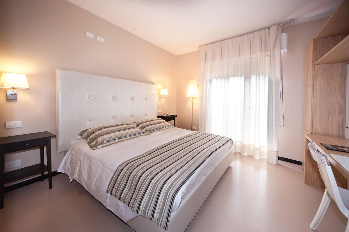 Una habitación de hotel con una cama grande, lámparas de noche, un escritorio y un armario.
