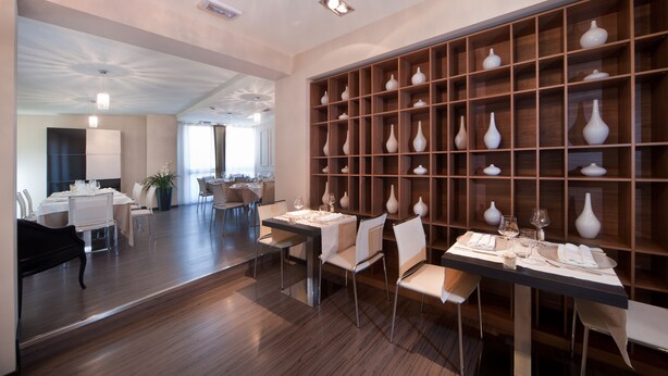 A modern dining area with a long table set for two, surrounded by chairs, and a wall of white vases.