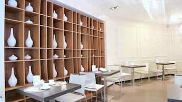 Un comedor moderno con estantes de madera que muestran jarrones blancos, mesas con sillas y una araña.
