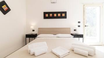 Habitación de hotel moderna con una cama grande, dos mesitas de noche con lámparas, un cabecero de madera y vistas a la vegetación a través de la puerta.