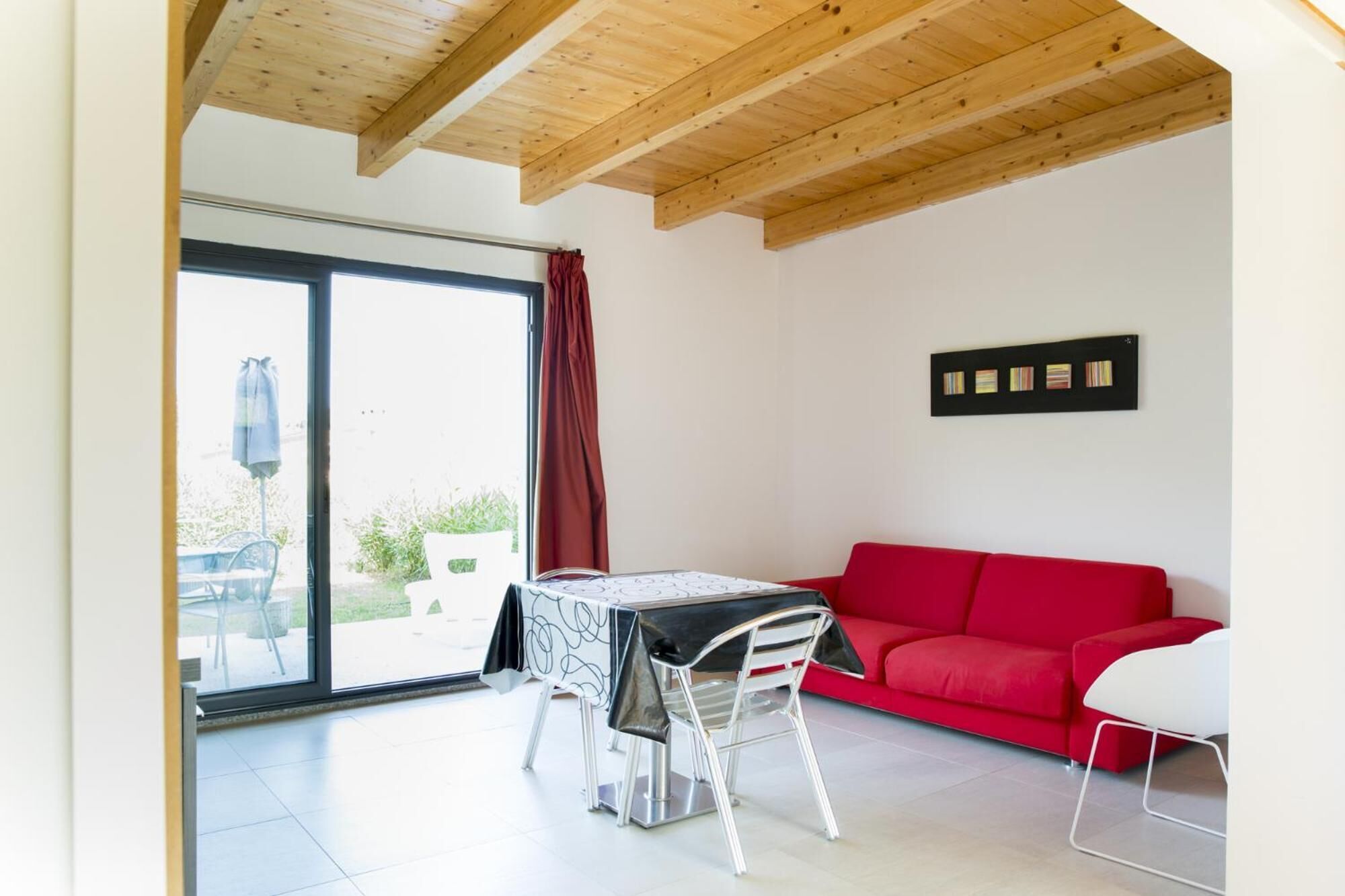 A modern living room with a red sofa, a dining table with chairs, and a large window with a view of greenery.