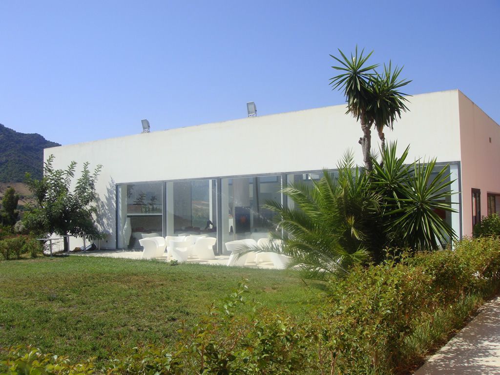 Een modern gebouw met grote glasramen, een plat dak en een verzorgd gazon met witte stoelen.