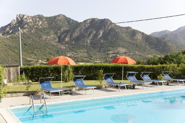 A swimming pool with lounge chairs and umbrellas, surrounded by mountains.