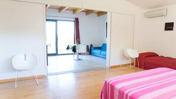 Una habitación moderna con suelo de madera, una cama con colcha a rayas rosas, una silla blanca, un sofá azul y una mesa con un jarrón de flores.
